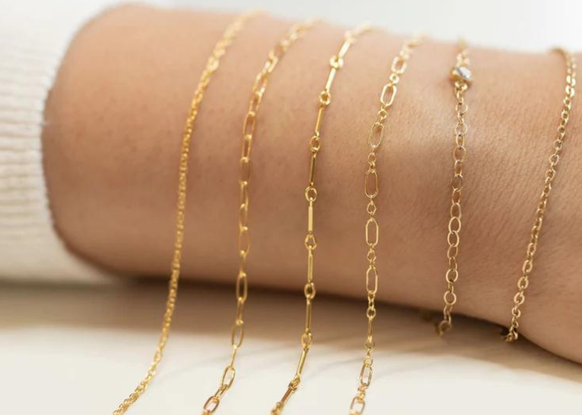 Gold chains displayed on a person's arm against a neutral background