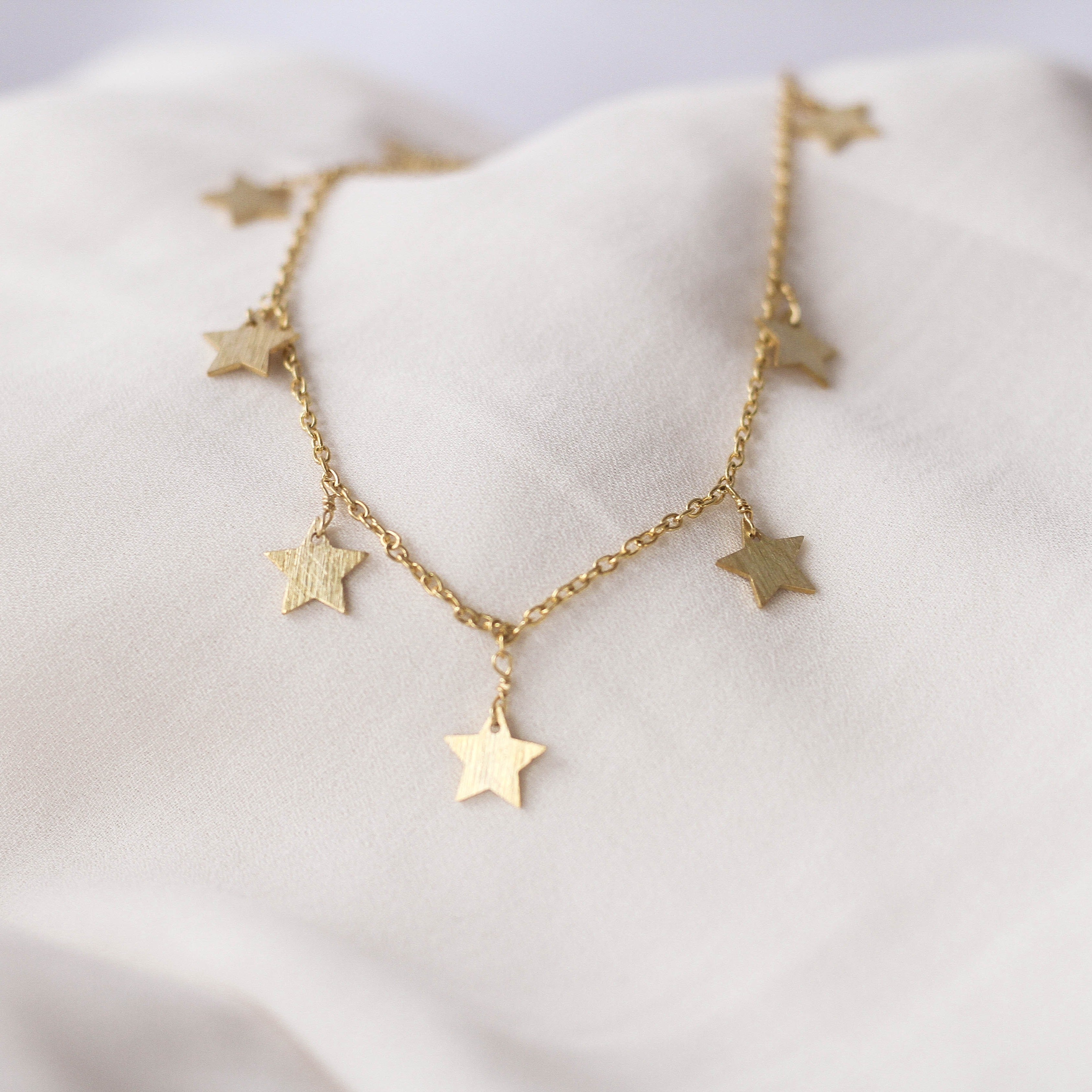 A gold-colored necklace with multiple star charms laid out on a white fabric surface.