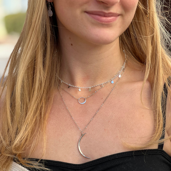 A person wearing a sterling silver tag necklace with a choker length, displayed along with other layered necklaces.
