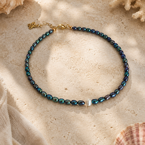 Anklet with peacock colored pearls and one white accent pearl on a sandy surface with shells and coral