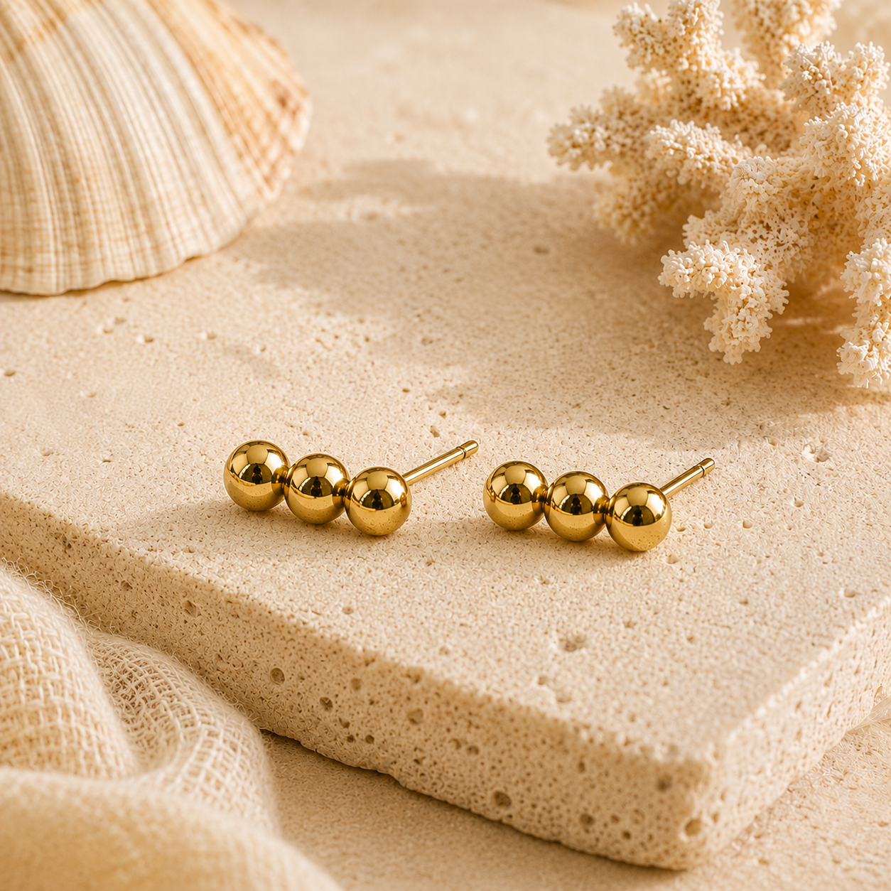 Gold stud earrings on a sandy surface with seashells and coral