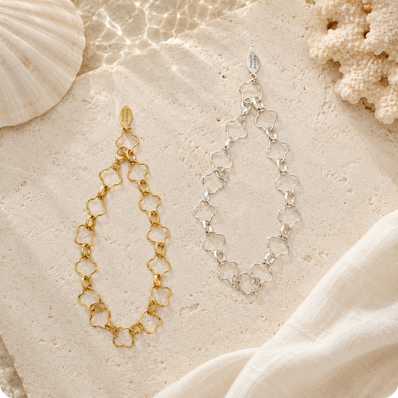 Gold and silver chain earrings on a sandy surface with shells and coral.