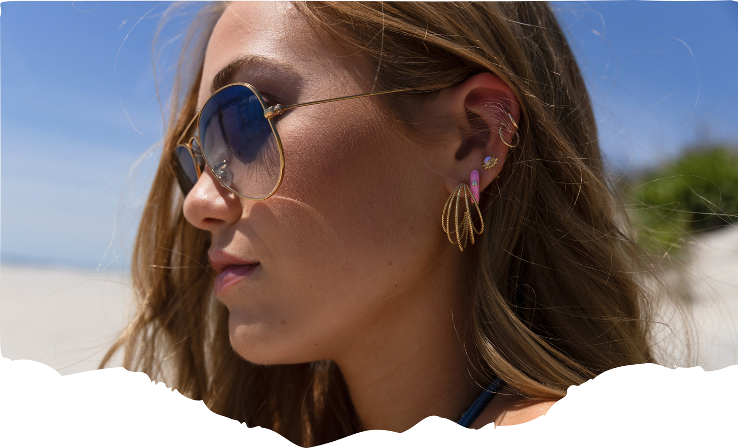 Woman wearing sunglasses and gold earrings on a beach