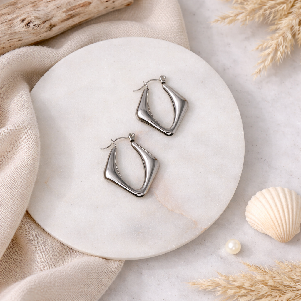 Silver hoop earrings on a marble surface with natural elements.