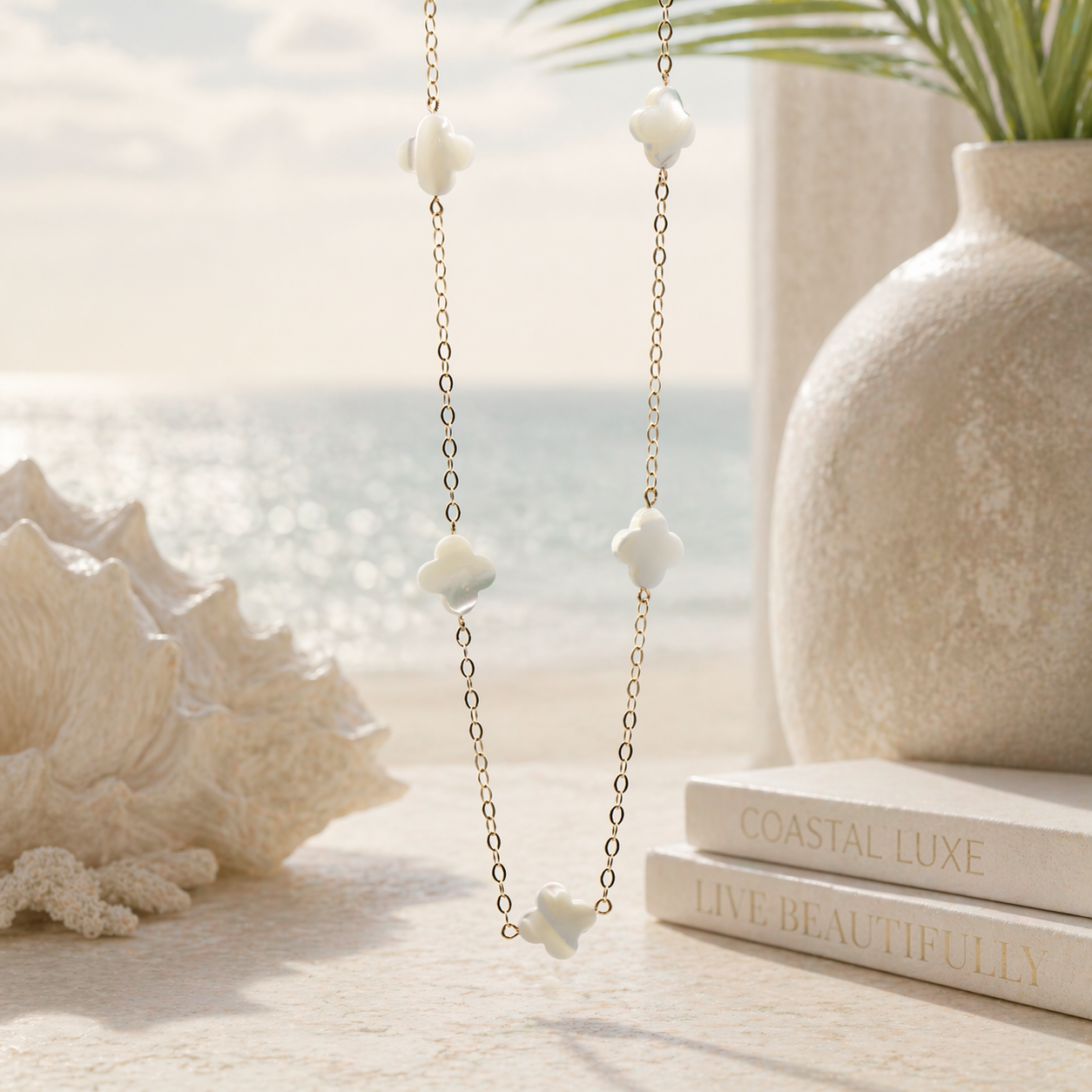 Necklace with shell pendants on a table with seashell, books, and plant in the background.