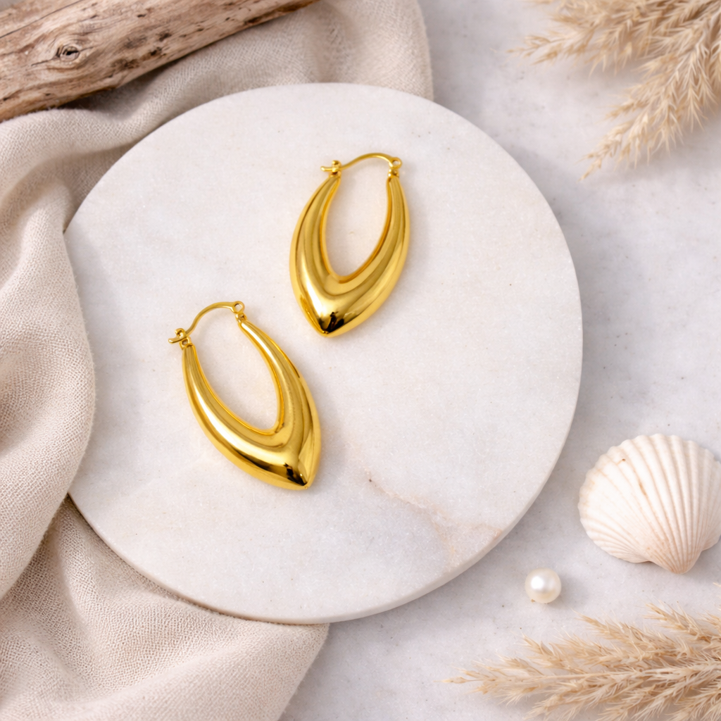 Gold hoop earrings on a marble surface with natural elements.