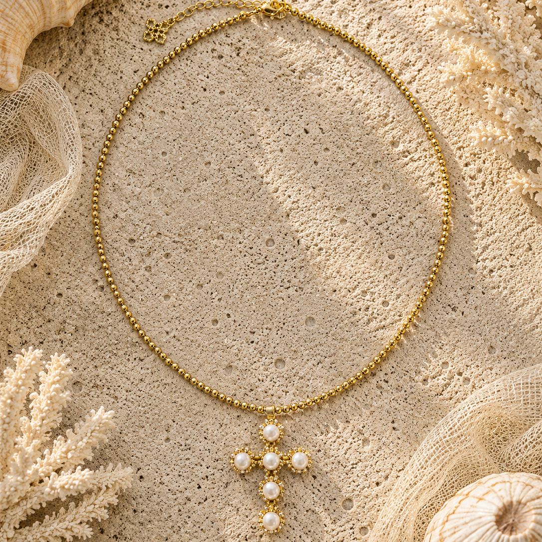 Gold necklace with a cross pendant on a sandy surface with shells and coral