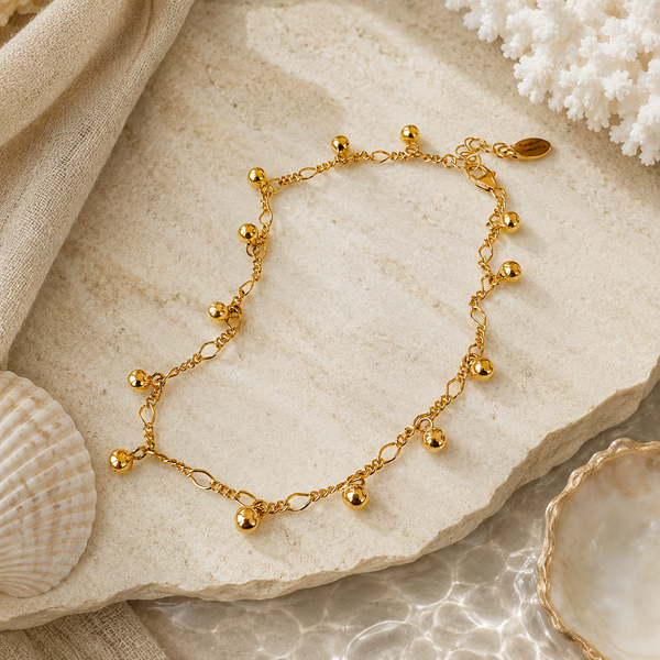 Gold anklet on a stone surface with shells and coral