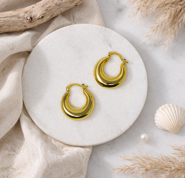 Gold hoop earrings on a marble surface with natural elements.