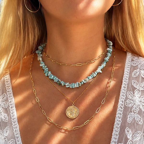 Close-up of a person wearing layered necklaces with a white lace garment.