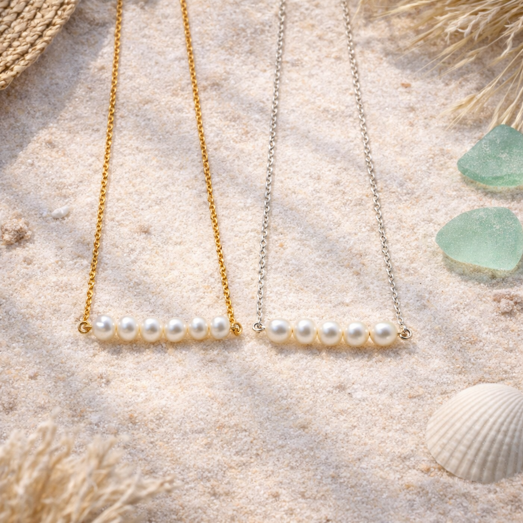 Pearl necklaces, on tin gold and one in silver, on a sandy surface with sea glass and shells