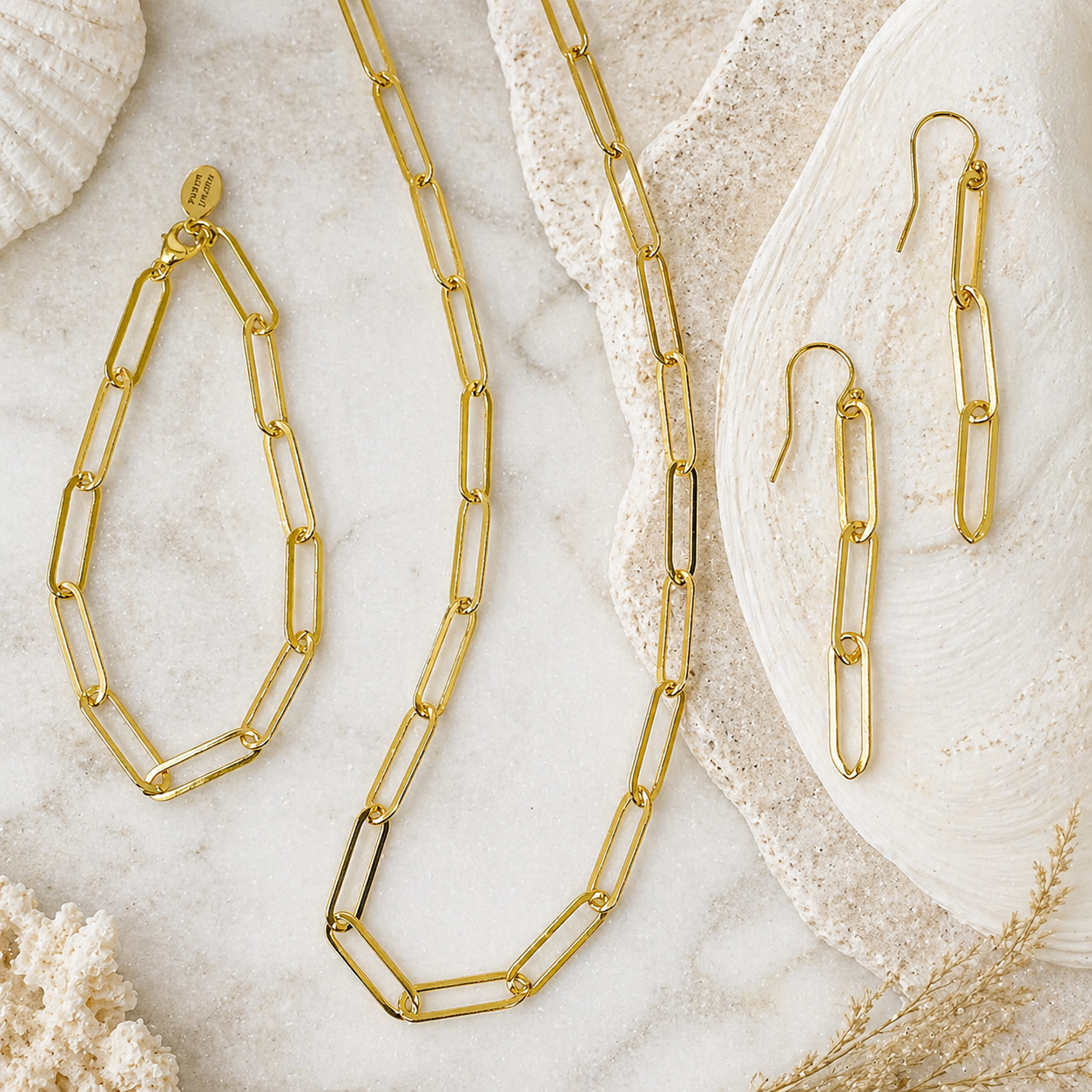 Gold chain necklace and earrings on a marble surface with seashells and coral.