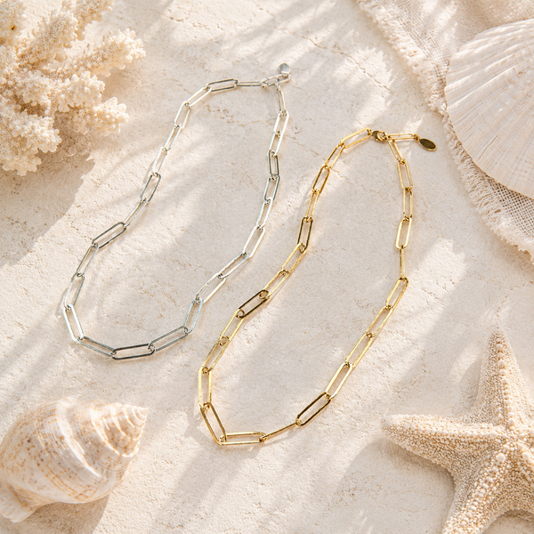 Two gold and silver chain necklaces on a sandy surface with shells and starfish.