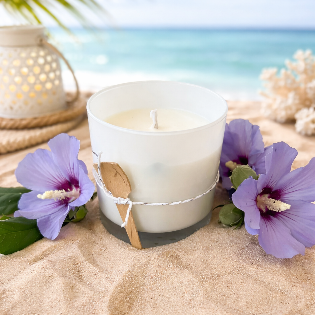 White candle with purple flowers on sand with ocean view