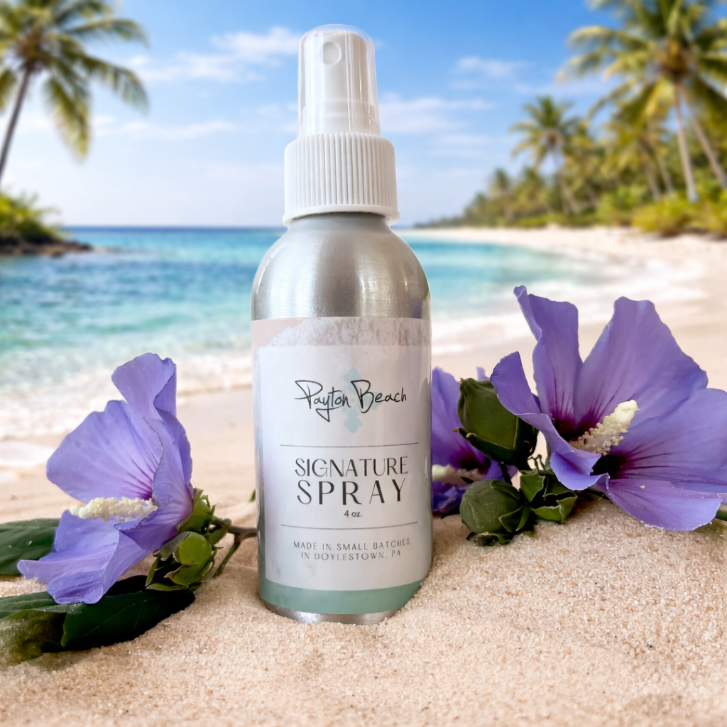 Bottle of 'Payton Beach' signature spray on a beach with purple flowers and palm trees in the background.