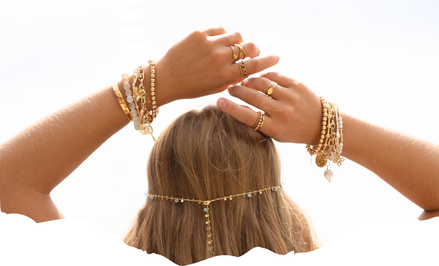 Two hands with gold  bracelets all stacked up being held over the models head.