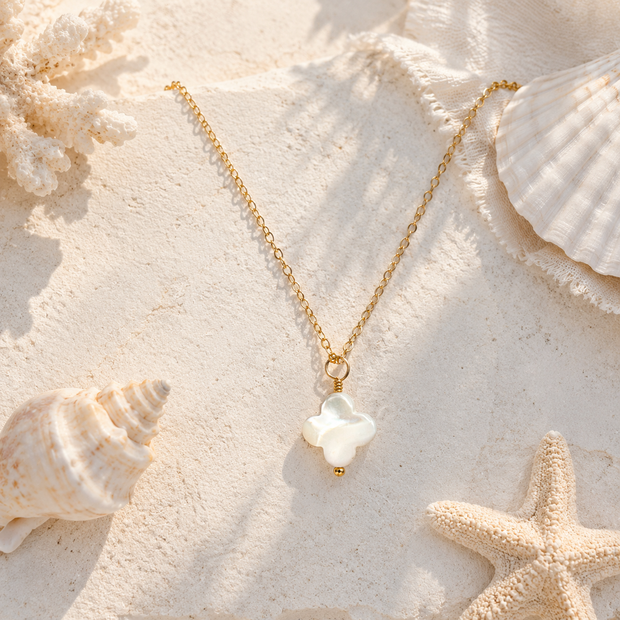 Gold necklace with a white pendant on a sandy surface with shells and a starfish.
