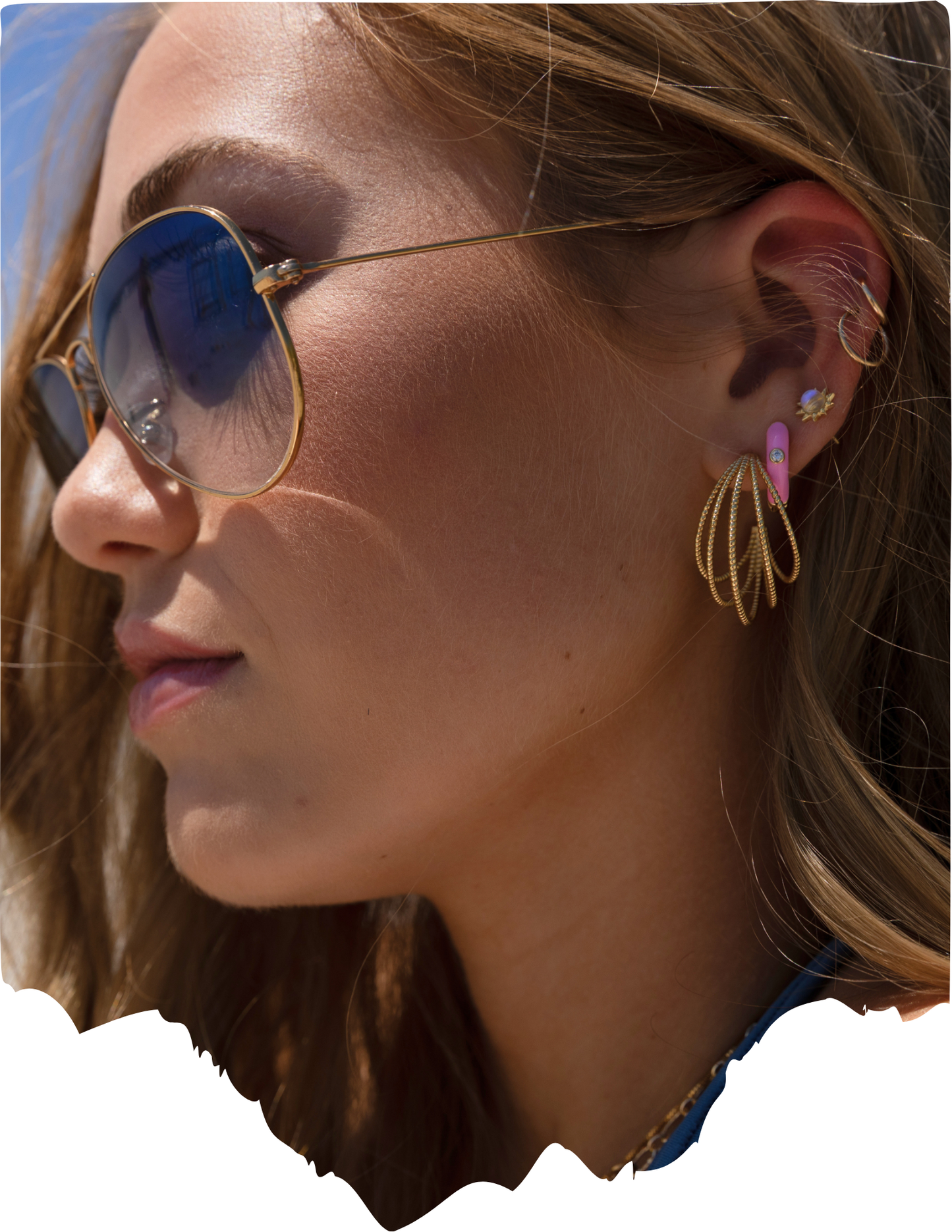 Close-up of a woman wearing sunglasses and gold hoop earrings with pink gemstones.