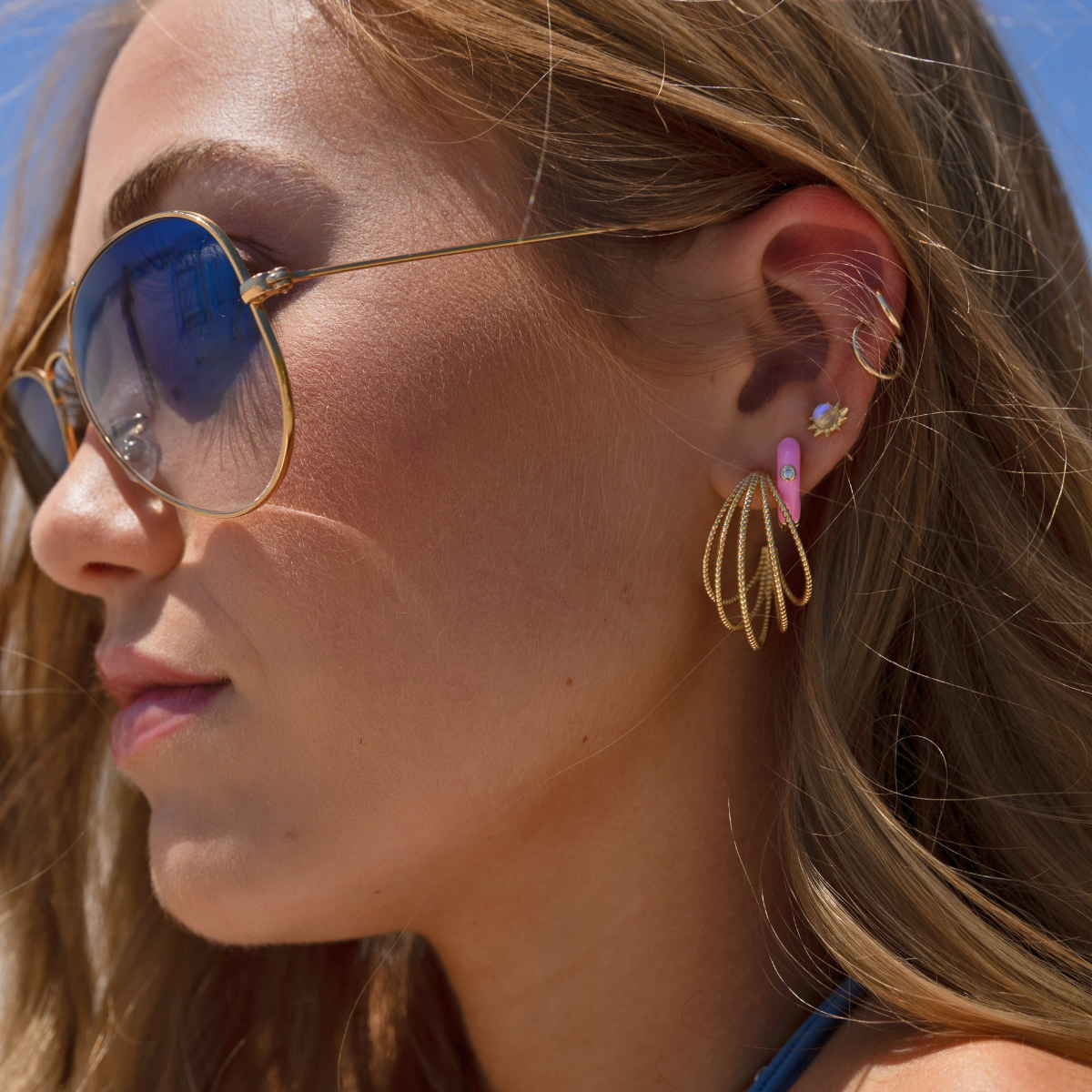 earring layer in gold with a multi layer textured hoop, a pink enamel huggie hoop, a sunflower moonstone stud and a petite classic hoop.