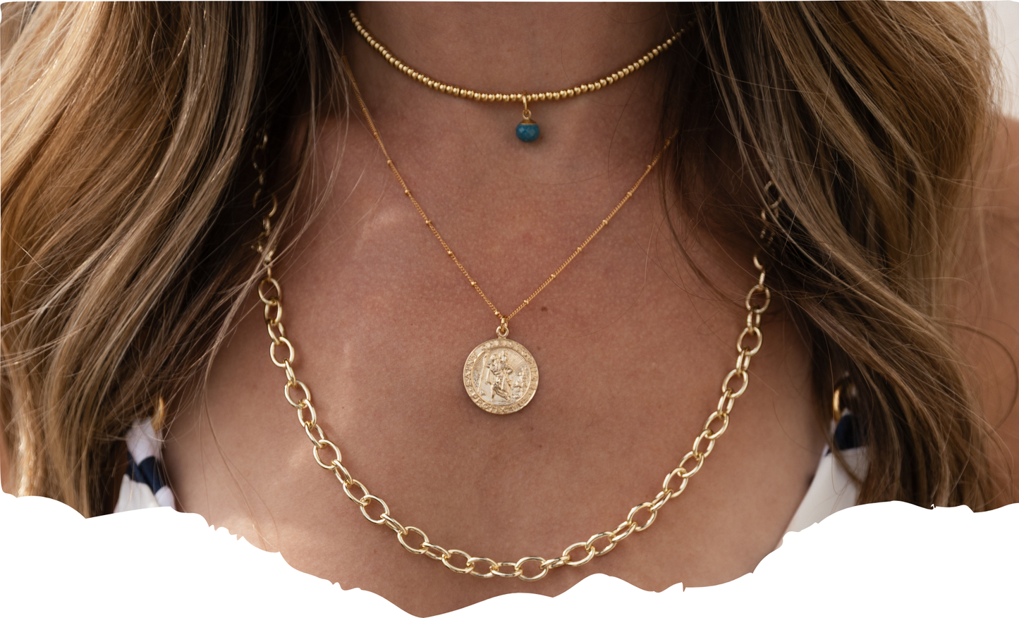 Close-up of a person wearing a gold necklace with a coin pendant on a plain background