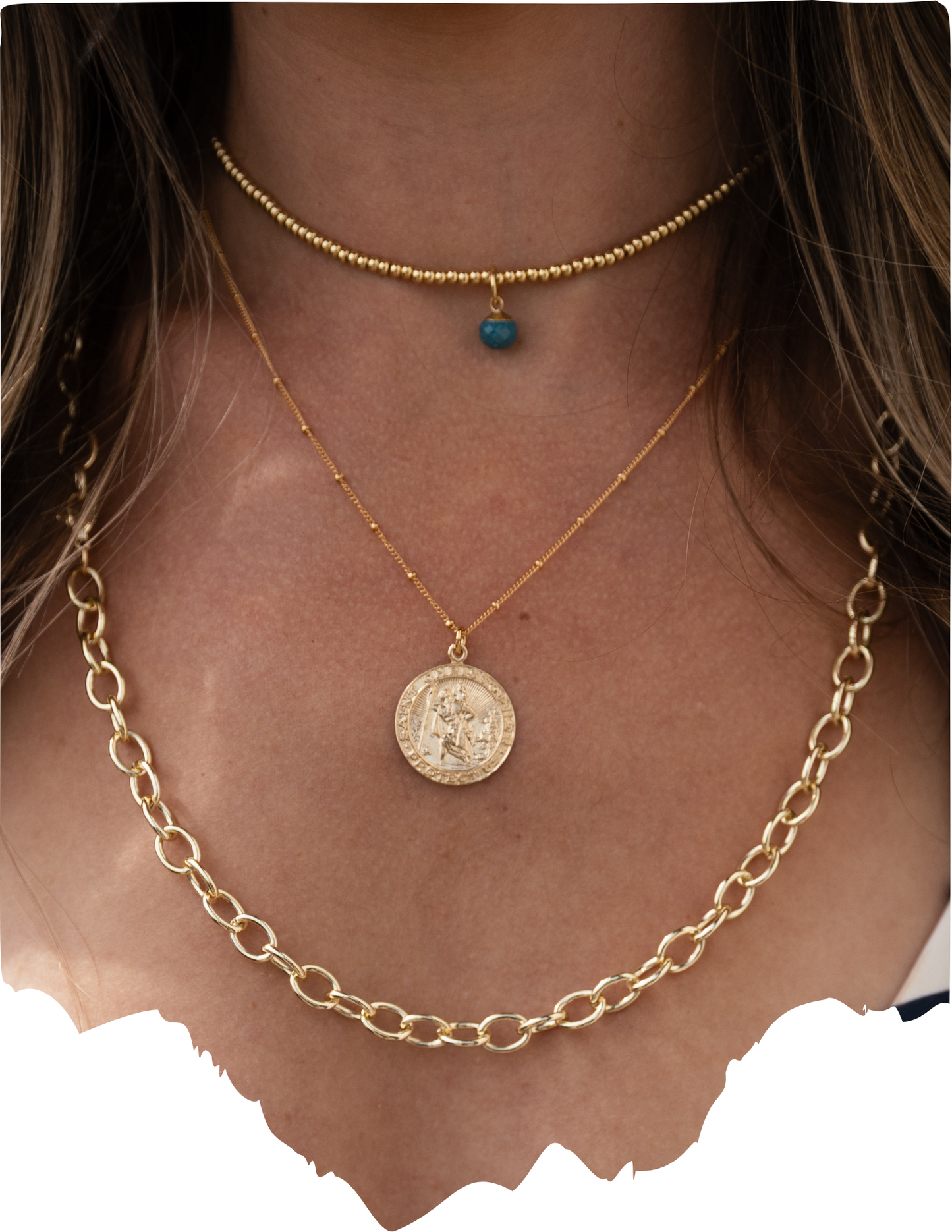 Close-up of a person wearing two gold necklaces with a coin pendant.