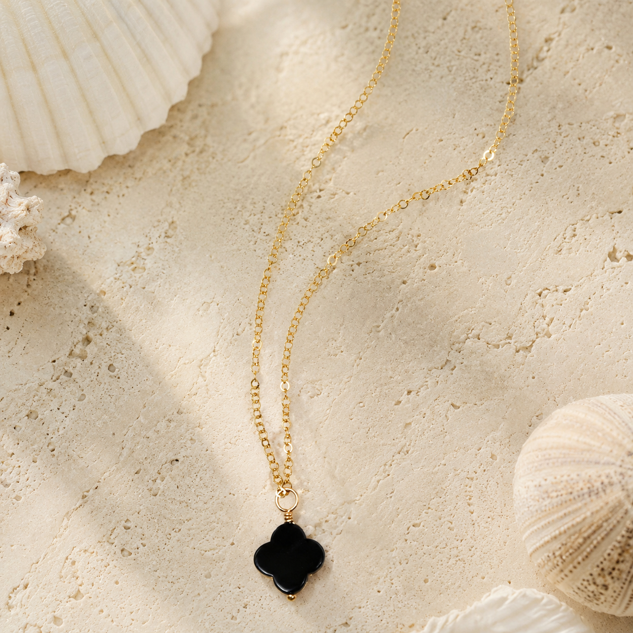 Fine gold chain with an onyx clover charm pendant on a white stone background.