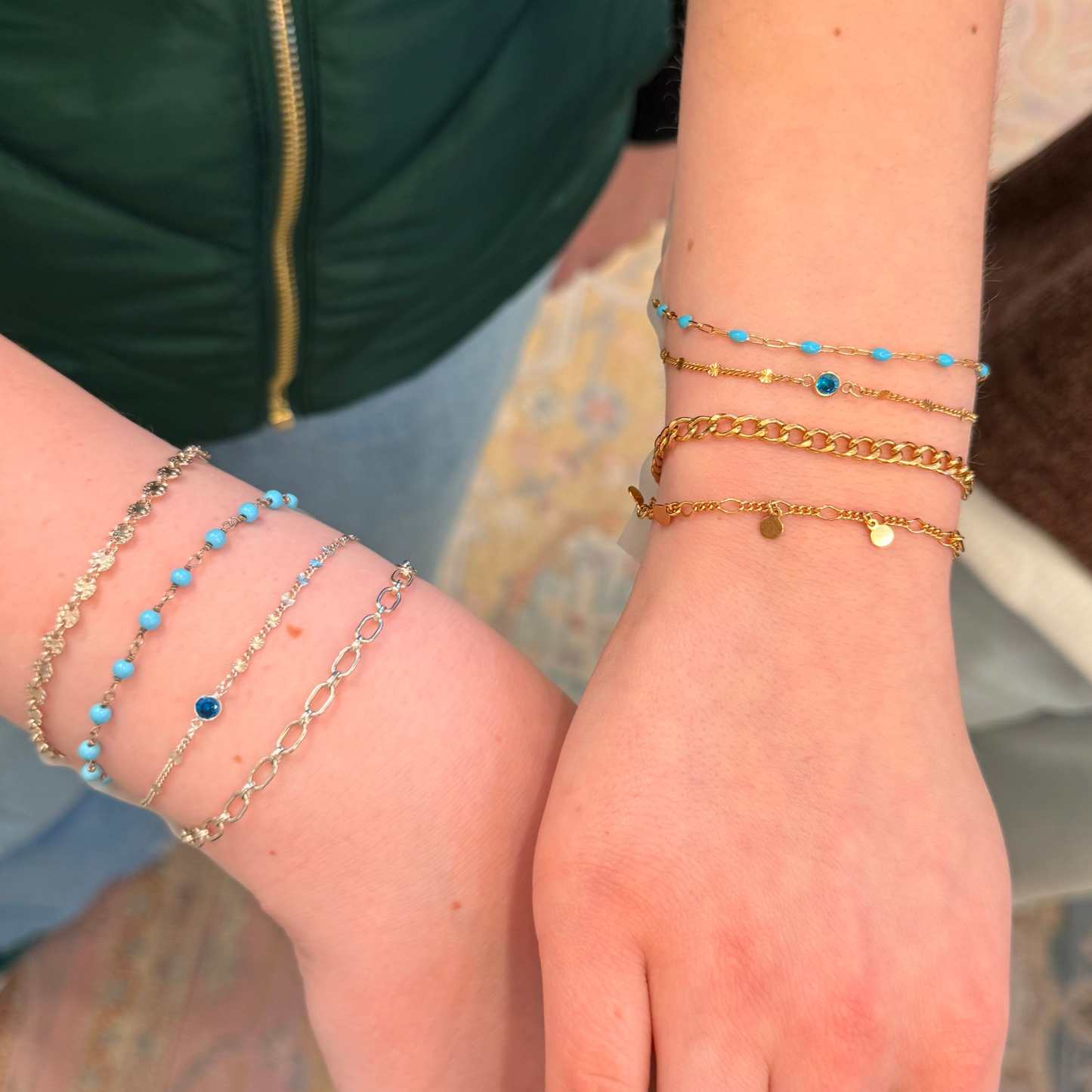 Close-up of a person's wrist with multiple permanent jewelry bracelets done at Payton Jewelry, two bracelets have birthstone connector charms in blue.