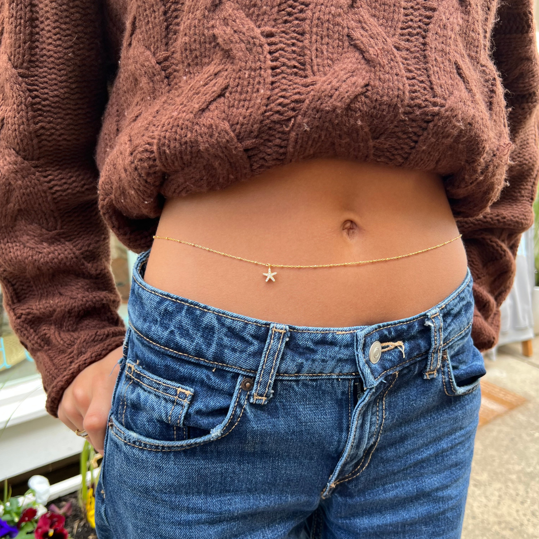 Person wearing a brown knitted sweater and blue jeans with a star-shaped pendant necklace.