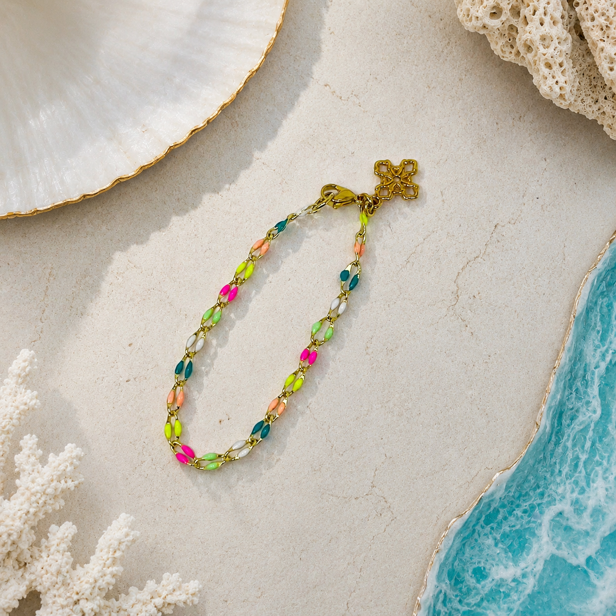 Colorful beaded necklace with a gold clasp on a sandy surface with ocean elements.