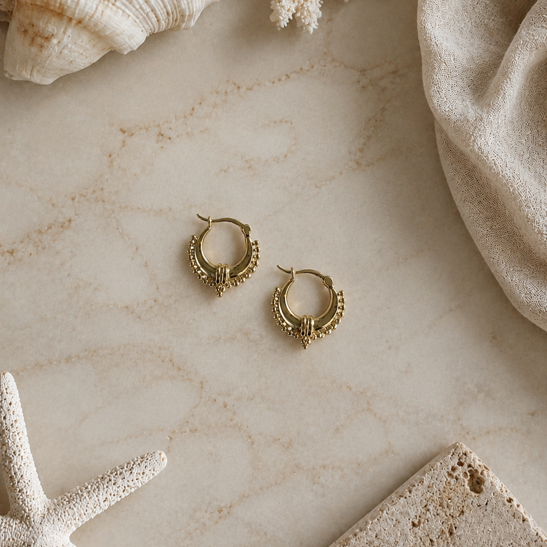 Gold hoop earrings on a marble surface with seashells and coral
