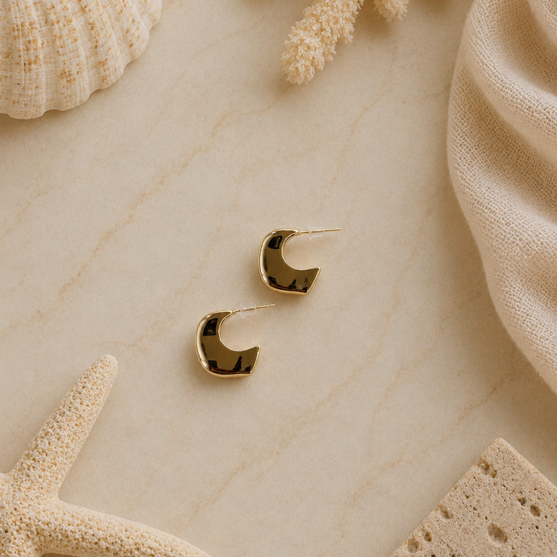 Gold hoop earrings on a textured beige surface with natural elements like a starfish and shell.