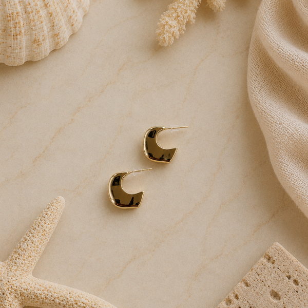 Gold hoop earrings on a textured beige surface with natural elements like a starfish and shell.