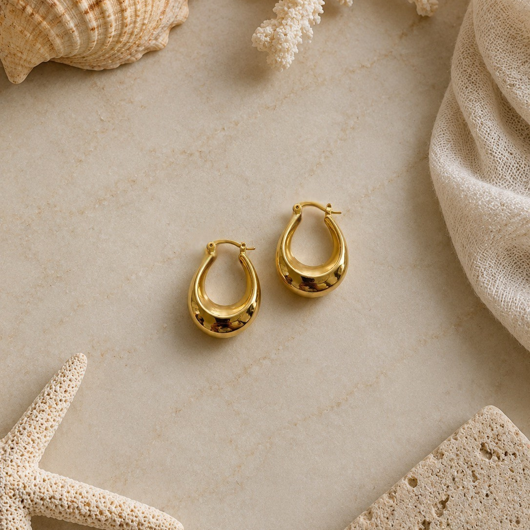Gold hoop earrings on a textured beige surface with natural elements.