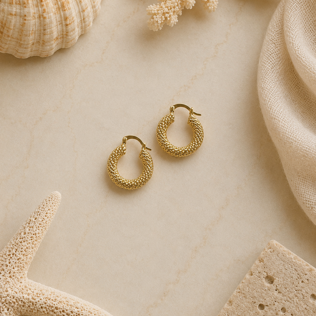 Gold hoop earrings on a textured beige surface with natural elements like a starfish and shell.