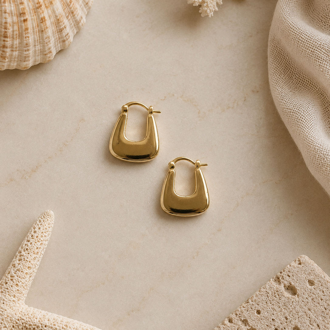 Gold hoop earrings on a marble surface with natural elements.