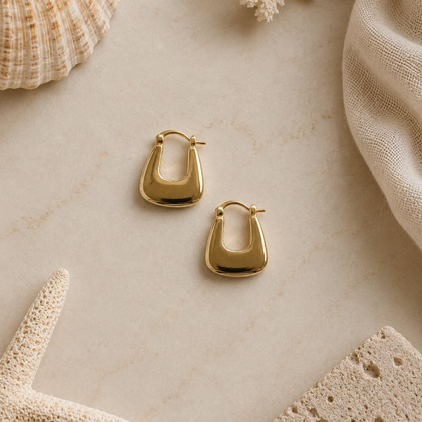 Gold hoop earrings on a marble surface with natural elements.