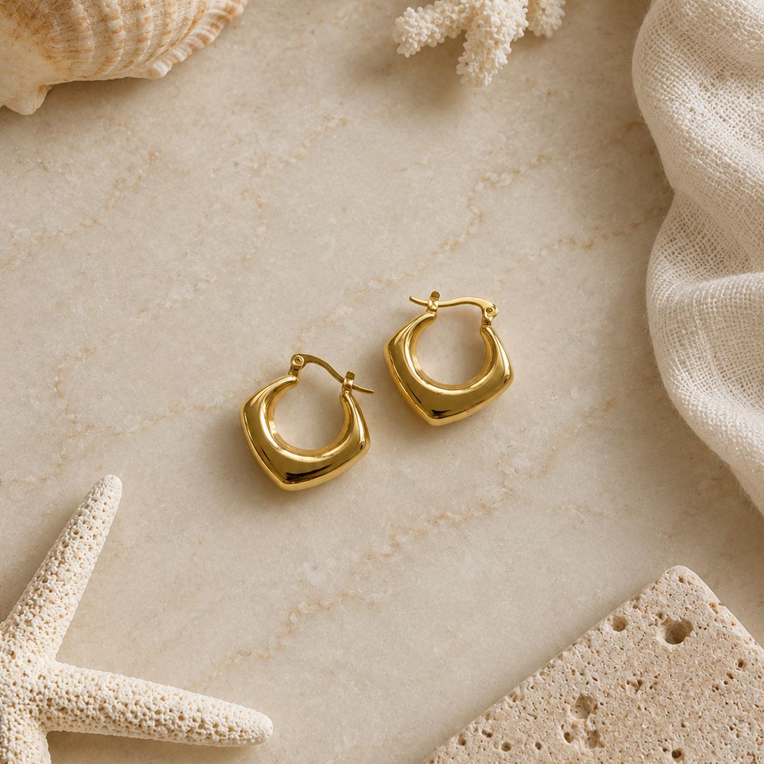 Gold hoop earrings on a textured beige surface with seashells and coral.