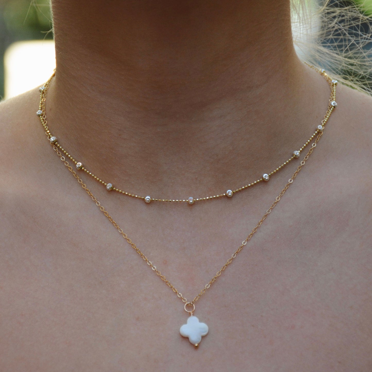 A gold-filled choker necklace with sterling silver beads layered over another chain with a sparkling pendant.