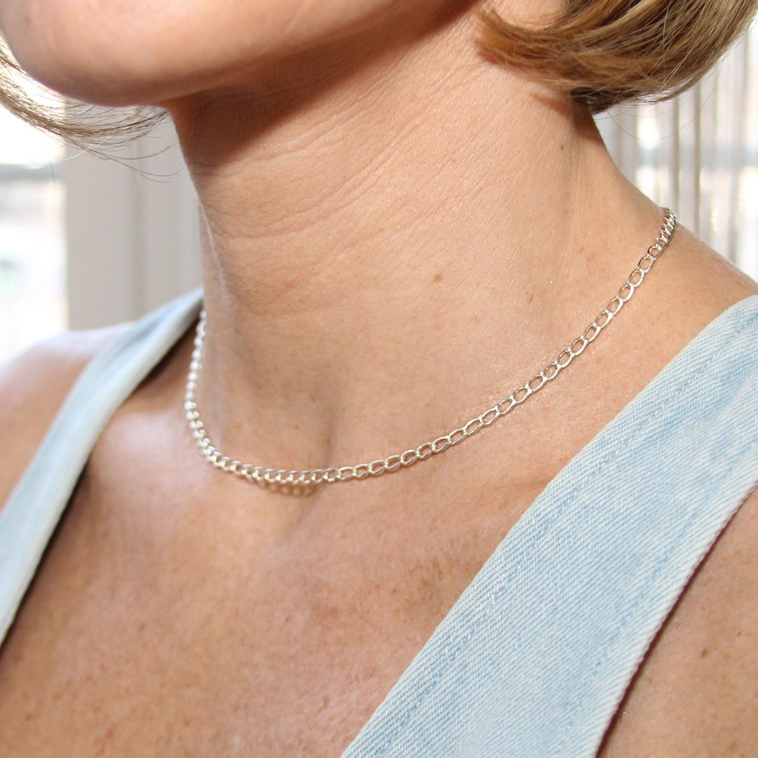 Silver curb chain necklace worn by a person with a light blue top.