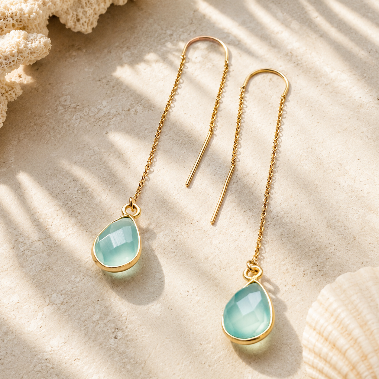 Gold threader earrings with an aqua green gemstone on a sandstone background.