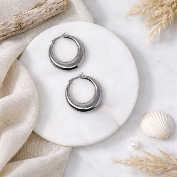 Silver hoop earrings on a white marble surface with natural elements.