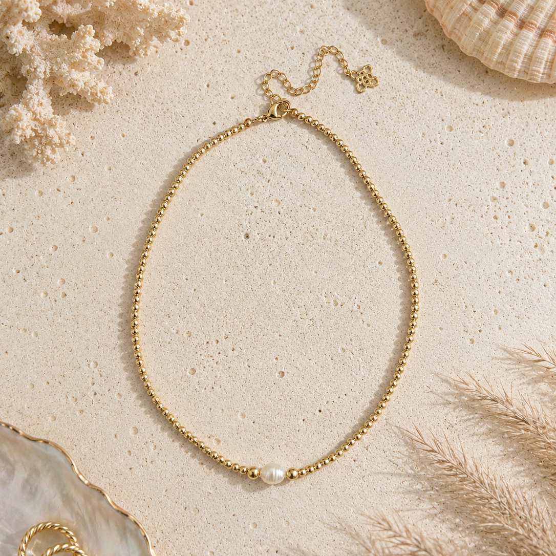 Gold necklace with pearls on a sandy surface with seashells and dried plants.