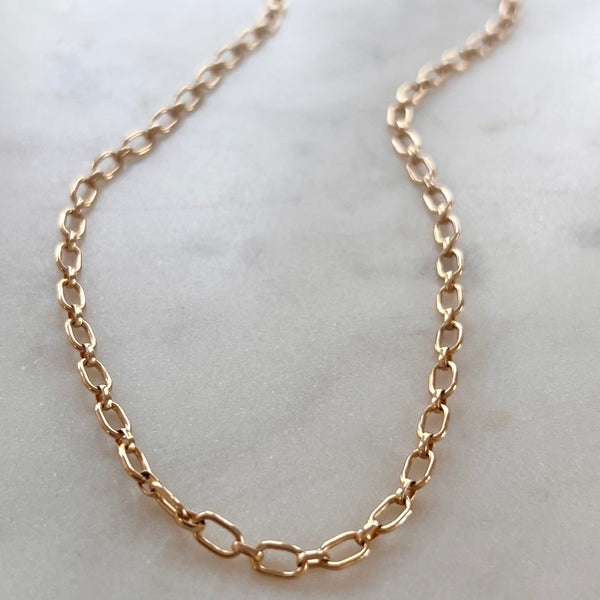 A gold-colored necklace laid out on a surface.