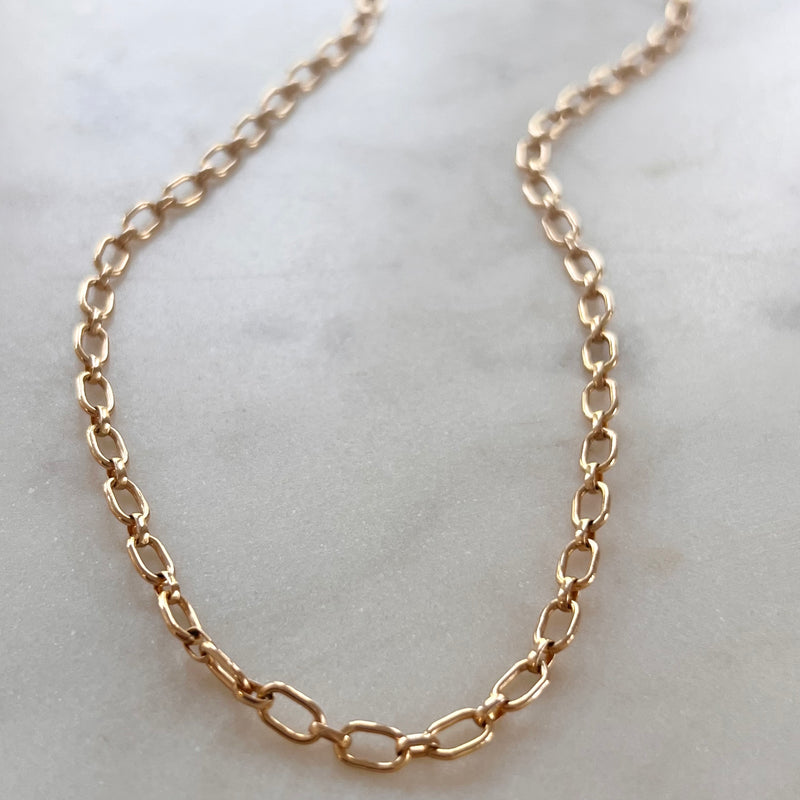 A gold-colored necklace laid out on a surface.