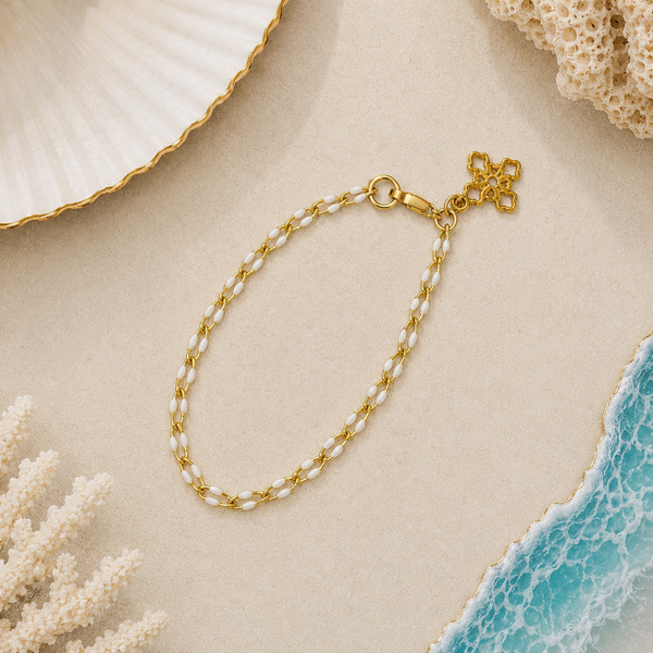Gold and white enamel chain bracelet on a sandy surface with shell and coral decorations.