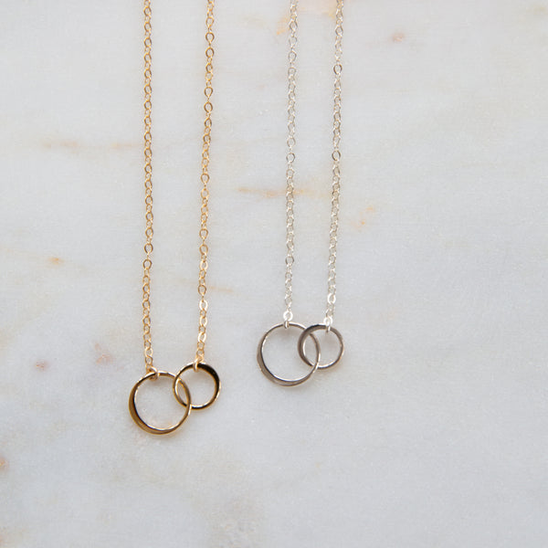 Two necklaces, one with gold chains and circles, the other with silver chains and circles, displayed on a marble surface.