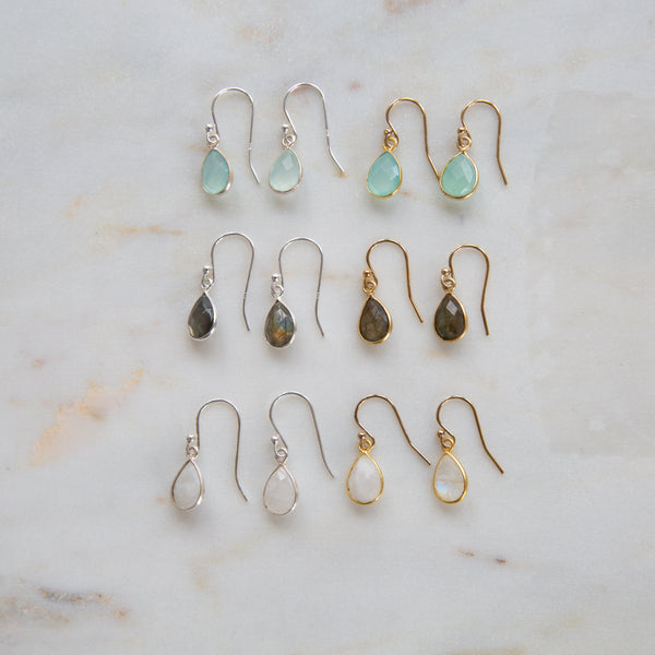 A collection of teardrop-shaped earrings in various colors, displayed on a marble surface.