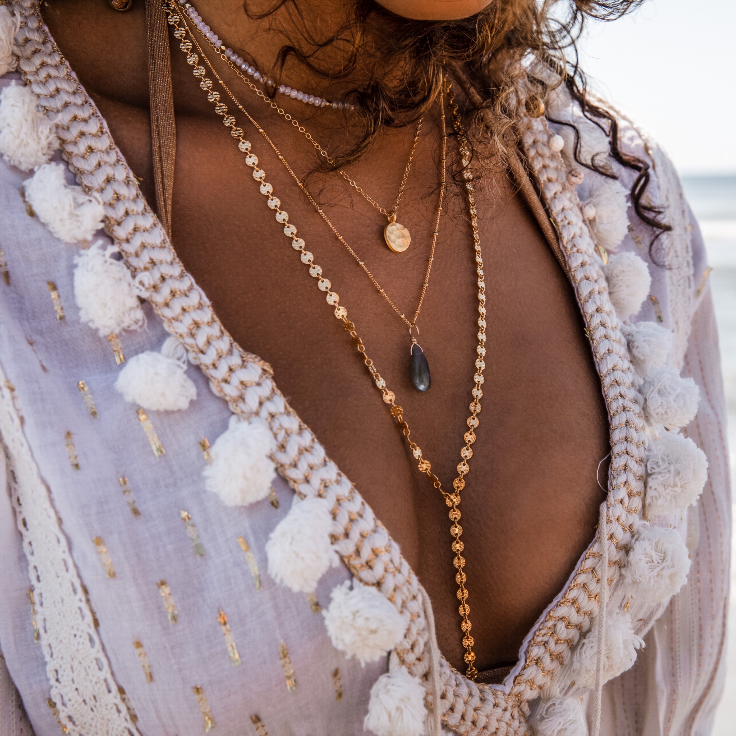 Coin drop necklace in gold layered with sacred elements necklace, hammered dot necklace, and a mermaid choker.