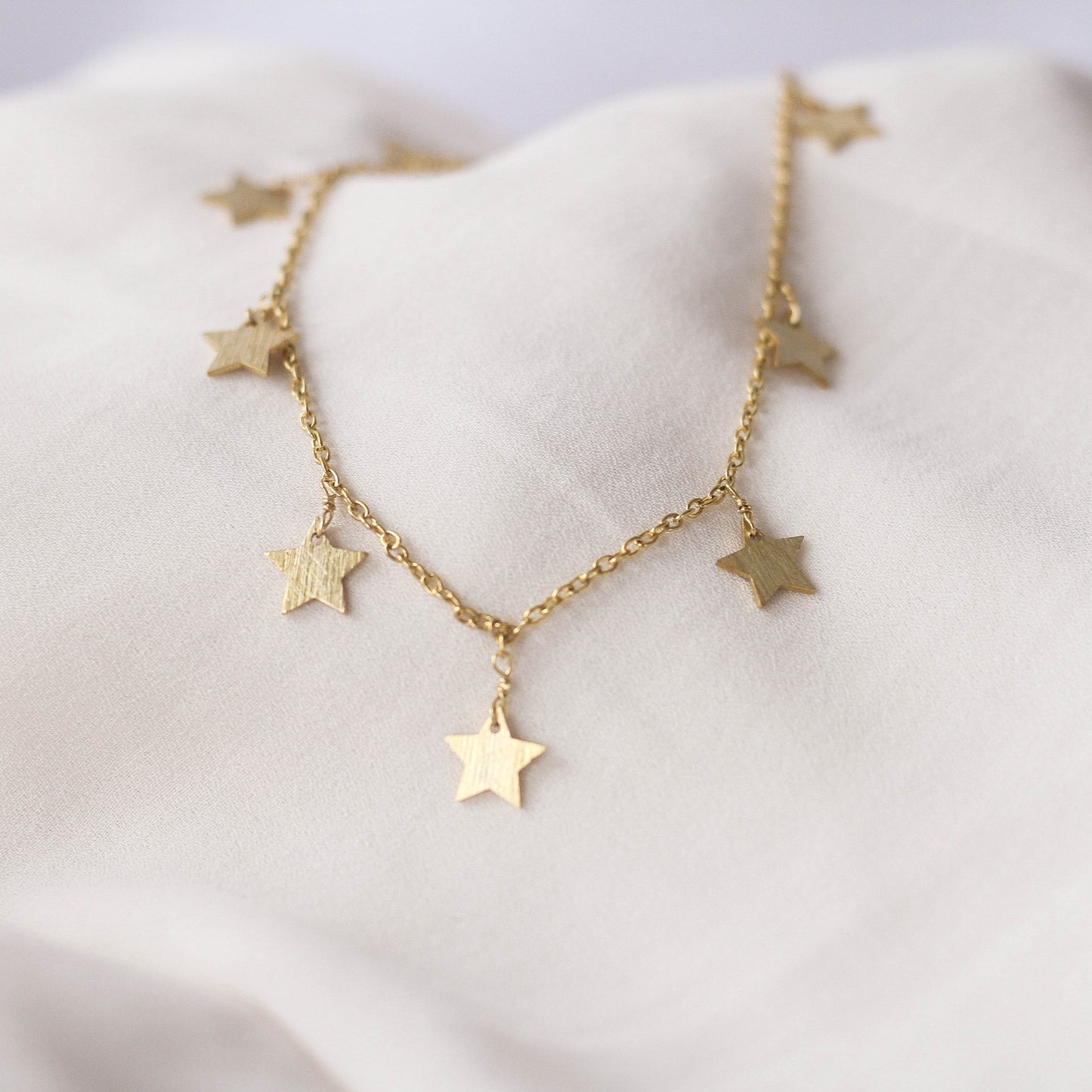 A gold-colored necklace with multiple star charms laid out on a white fabric surface.