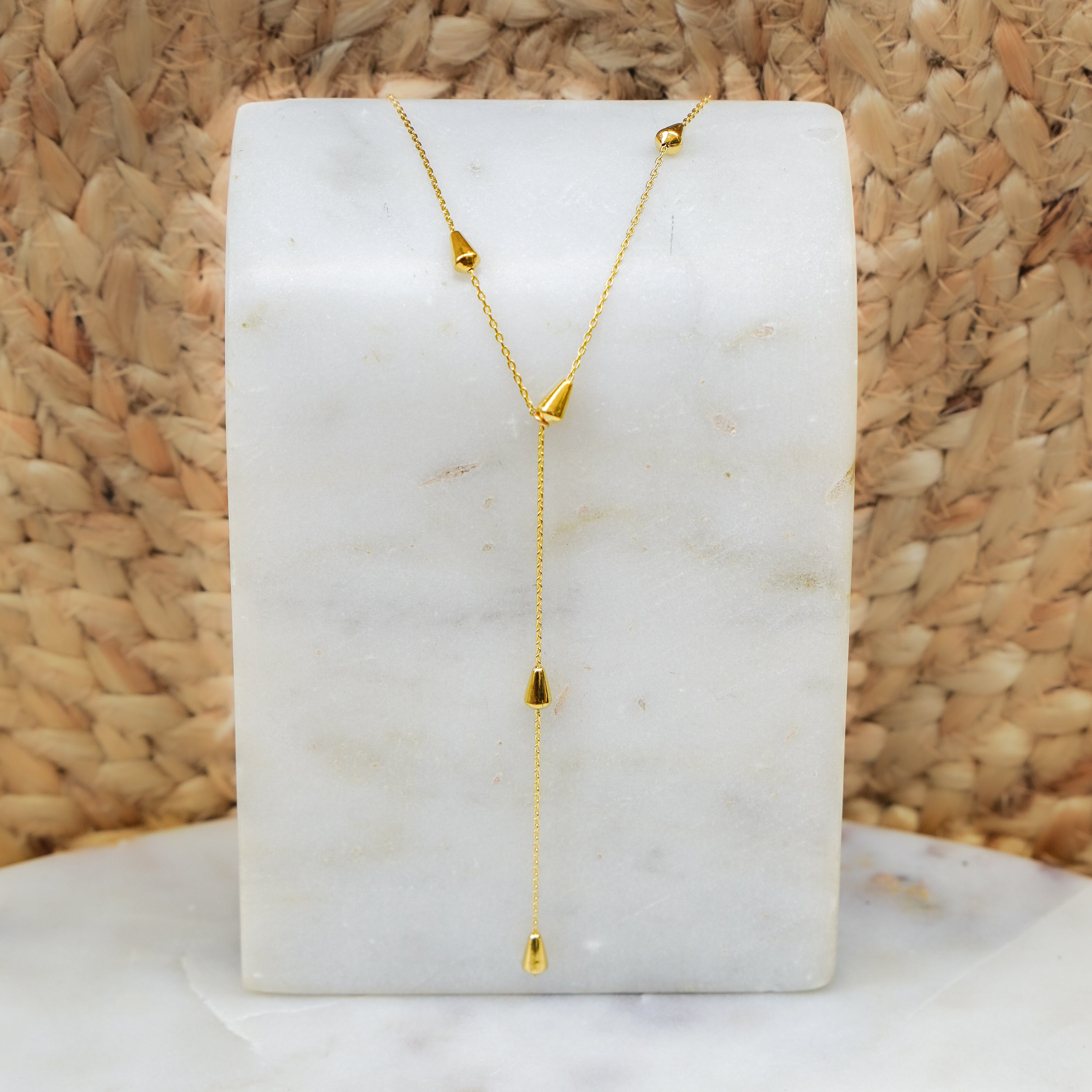 A gold drop necklace with triangle teardrop pendants displayed on a white marble surface.